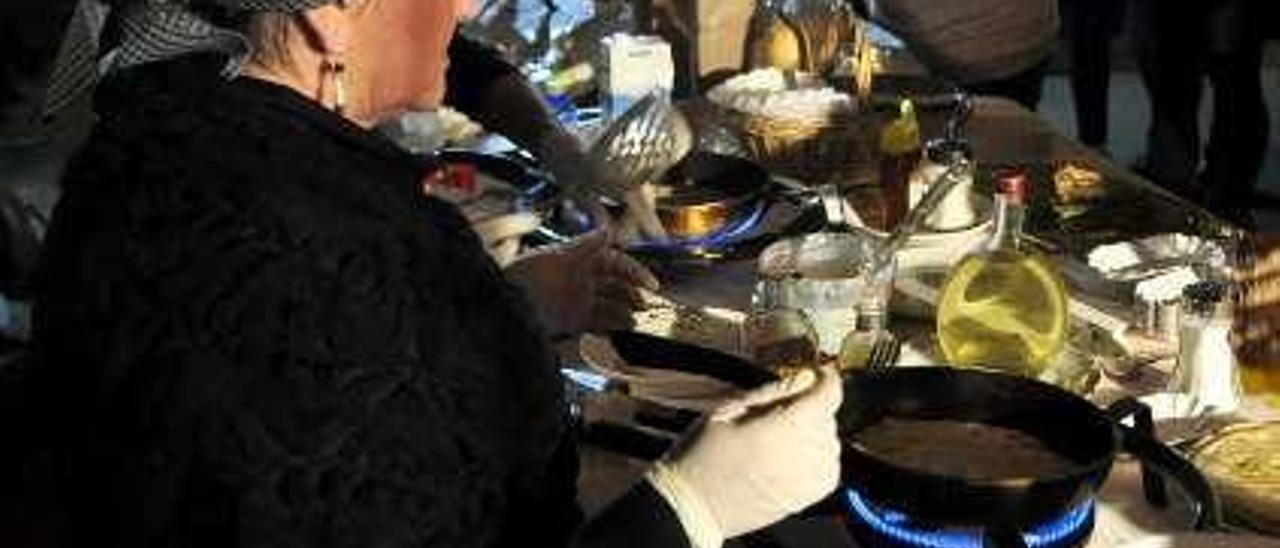 Los vecinos, durante el esfoyón. A la izquierda, Raquel Menéndez, preparando los frixuelos el sábado por la noche en Almuña.