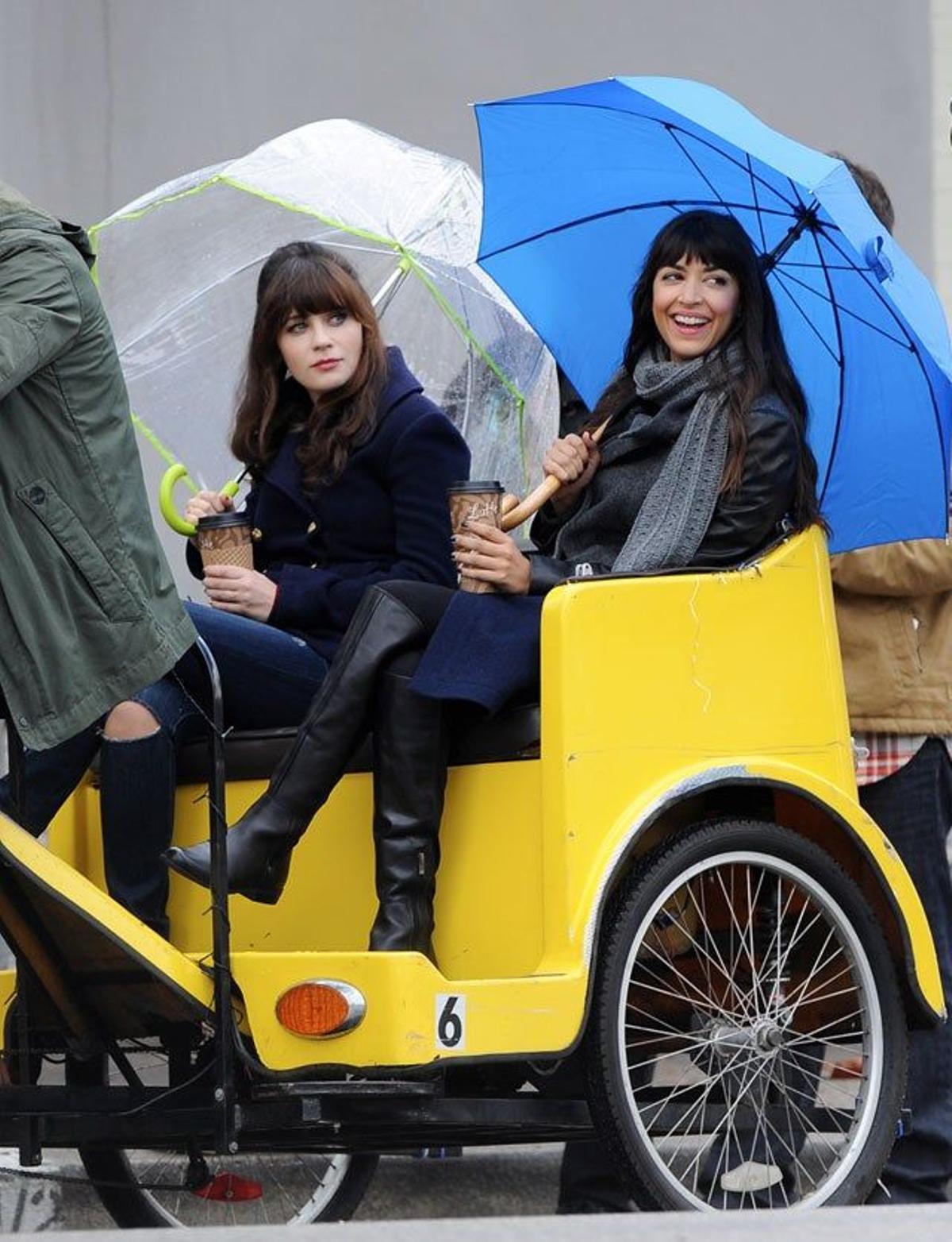 Zooey Deschanel y Hannah Simone en un pedicab con paraguas