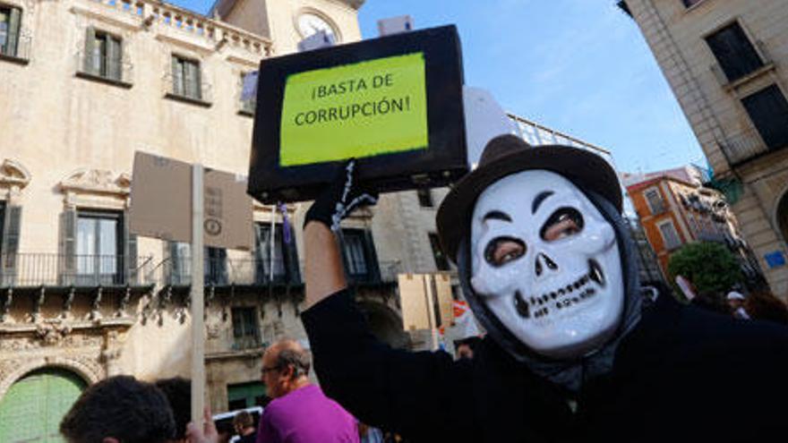 Una persona protesta con una máscara y una pancarta ante el Ayuntamiento de Alicante