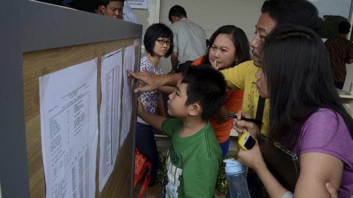 Familiares de los pasajeros del vuelo desaparecido miran una lista en el aeropuerto de Surabaya, este domingo.