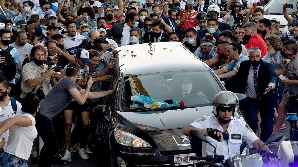 Fans apiñados junto al coche fúnebre que transporta a la leyenda del fútbol argentino Diego Armando Maradona en su camino desde el palacio presidencial de la Casa Rosada al cementerio, en Buenos Aires, el 26 de noviembre de 2020