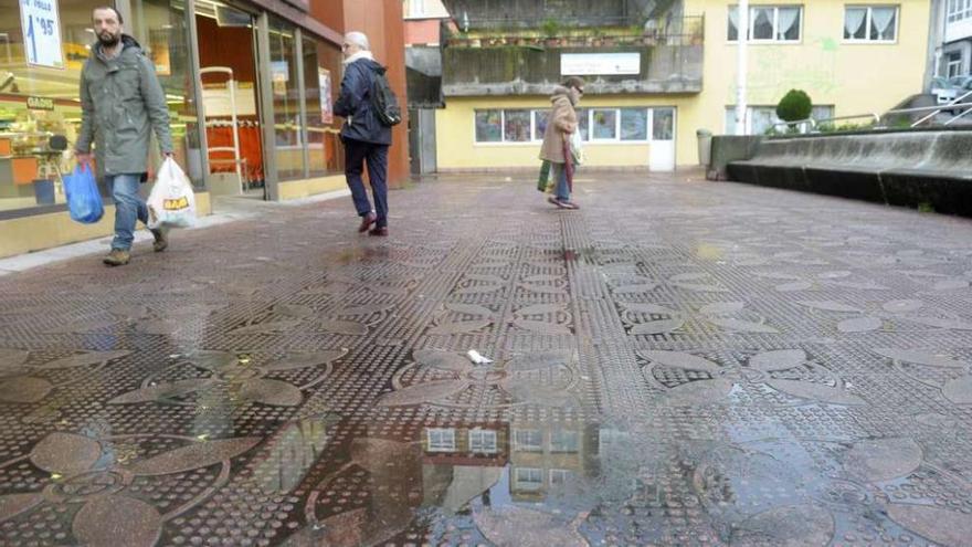 Baldosas mojadas y con suciedad en la plaza de Monte Alto, con la escuela infantil municipal al fondo.