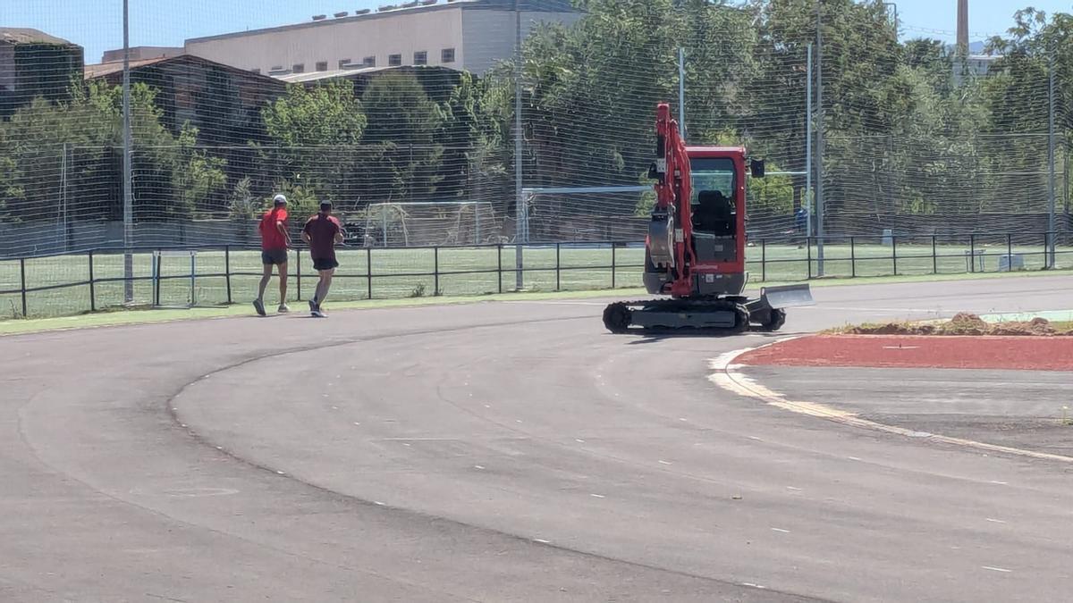 Una imagen de este jueves con una máquina trabajando y dos atletas rodando por la pista