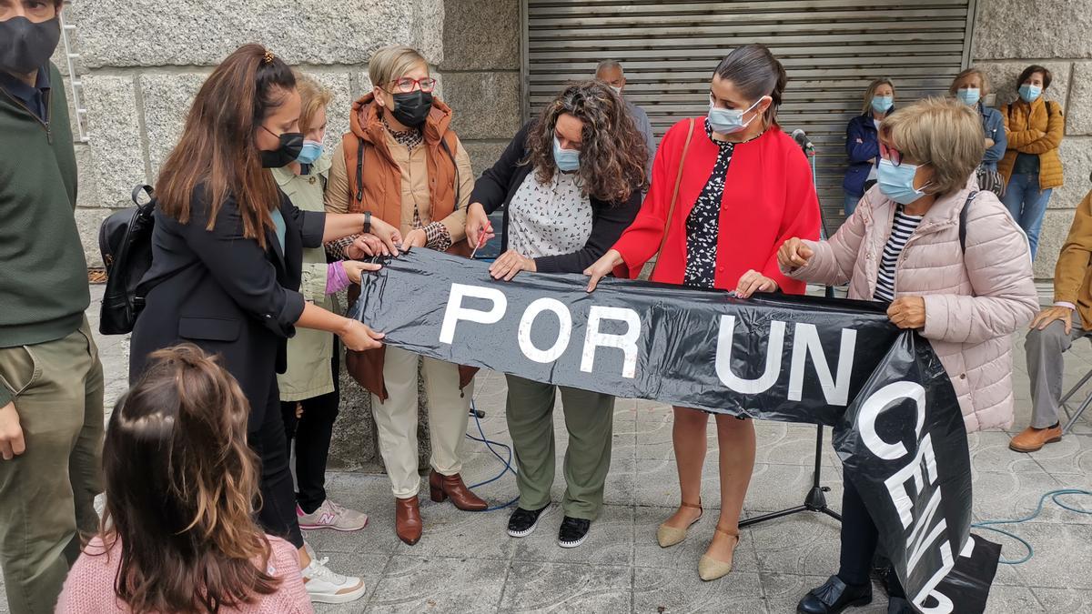 La alcaldesa, Leticia Santos, (de rojo) observa como la edil María Ortega trocea la pancarta negra de la Plataforma da Sanidade ante la Casa del Mar y con otros ediles y Cocha Trigo a su lado.