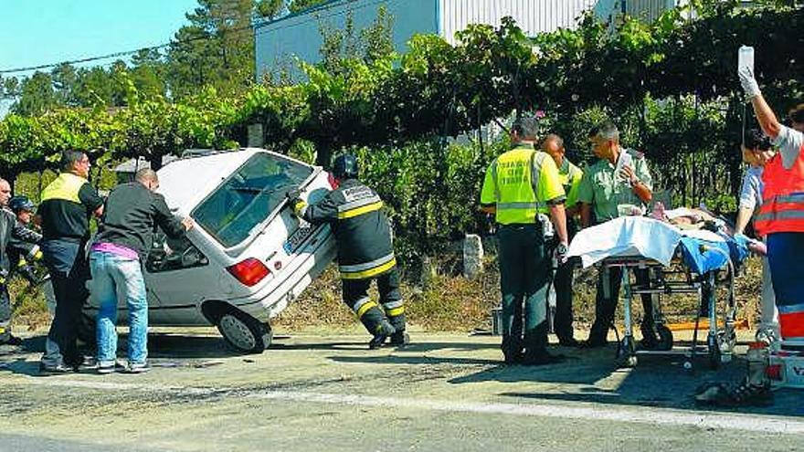 Vecinos y bomberos enderezan el coche, mientras los sanitarios atienden al herido de Ponteareas. / e. álvarez