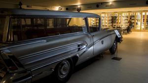 Al fondo, Adrià Terol consulta unos libros en la biblioteca funeraria instalada en el cementerio de Montjuïc, junto a la colección de carrozas fúnebres. En primer plano, un Buick del 58 con su ataúd.