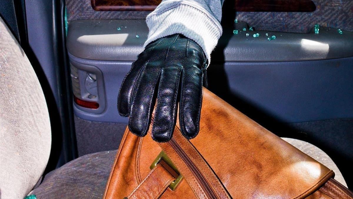 Un ladrón sustrae un bolso de un asiento.