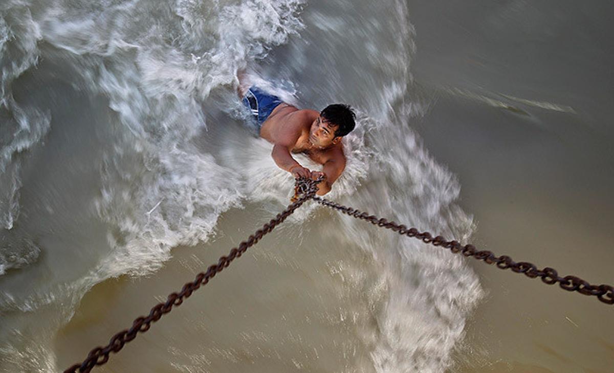 Un home penjat d’unes cadenes subjectes a un pont es banya en les aigües del riu Ganges a Haridwar, Índia.
