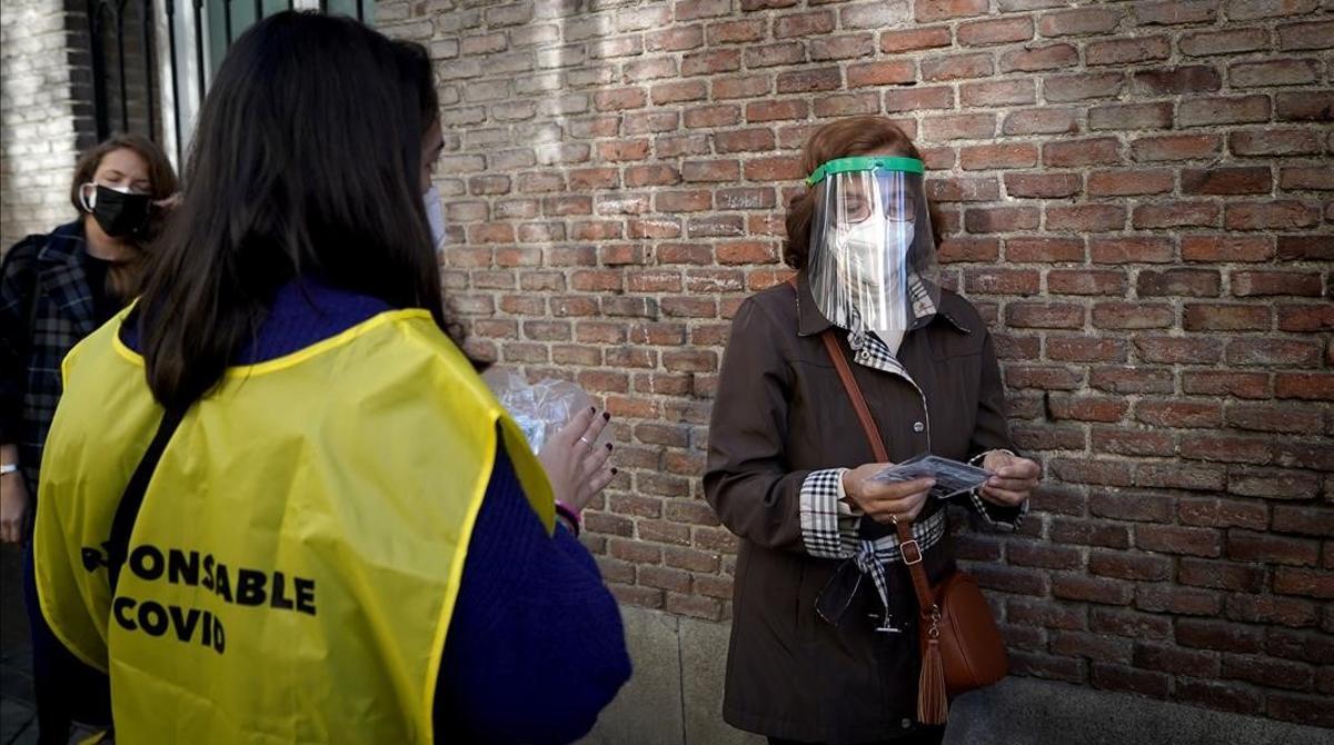 Entrega de mascarillas en la cola de un colegio electoral de Madrid.