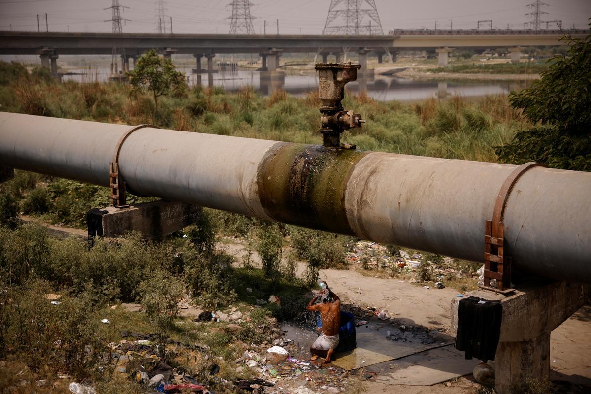 Un hombre se baña bajo una tubería de agua rota, en un día de calor extremo en Nueva Delhi.