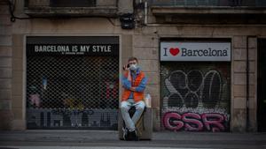 Archivo - Un hombre escucha a su teléfono móvil frente a dos tiendas turísticas en Barcelona.