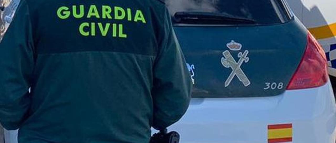 Archivo - Un agente de la Guardia Civil de espaldas y junto a un vehículo oficial del cuerpo.