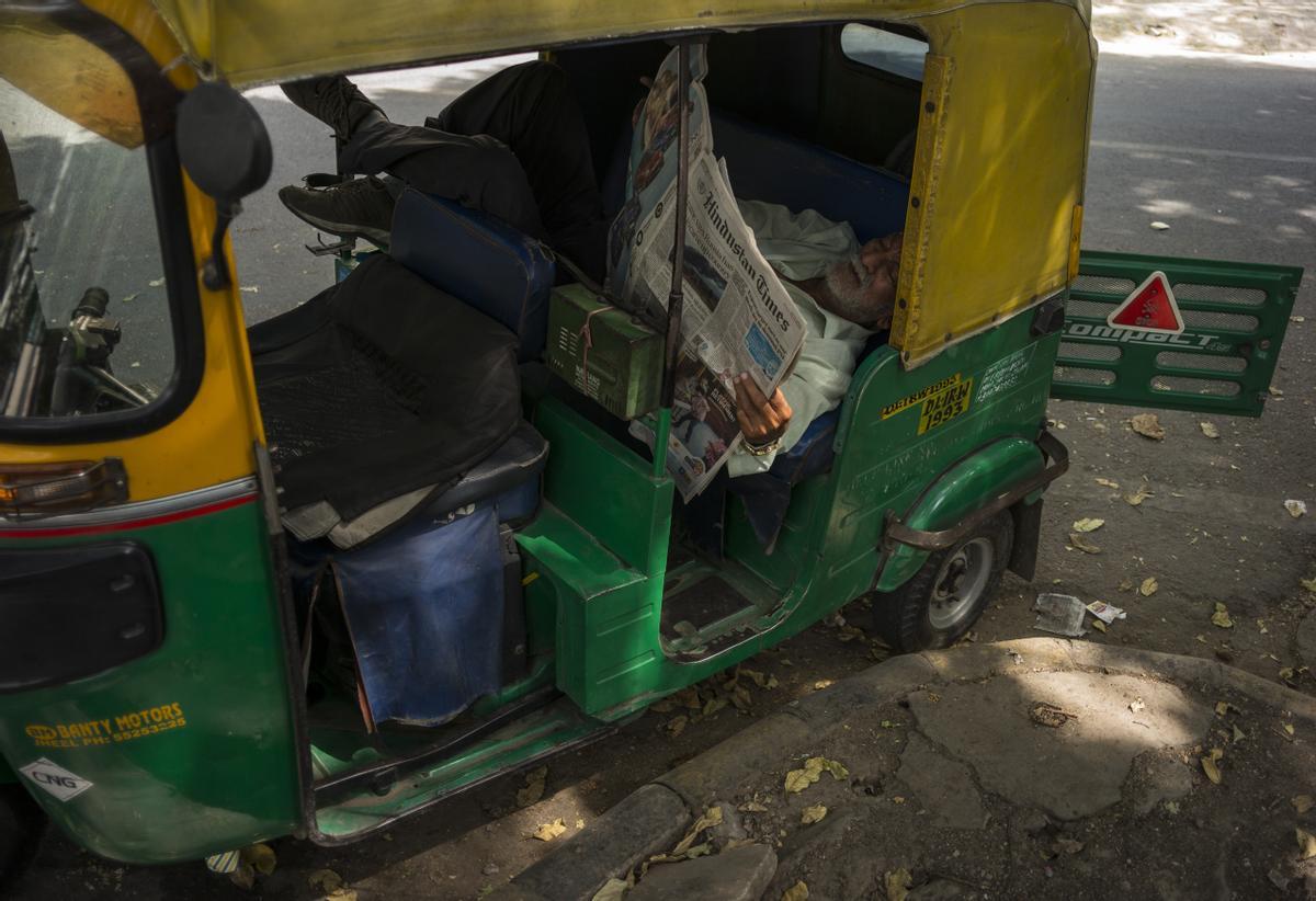 Un conductor de rickshaw descansa con su vehículo aparcado a la sombra de un árbol, en una calle de Nueva Delhi.