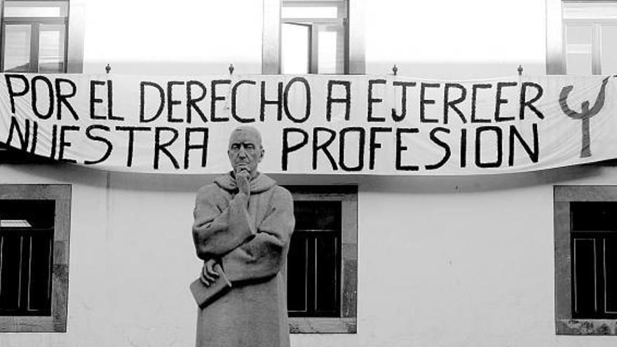 Una pancarta cuelga del edificio de la Facultad de Psicología. En primer término, la escultura del Padre Feijoo.