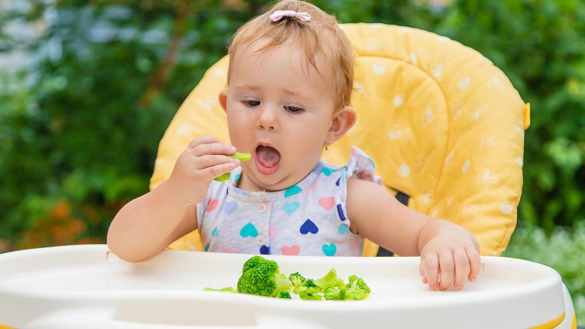 Una bebé comiendo brócoli.