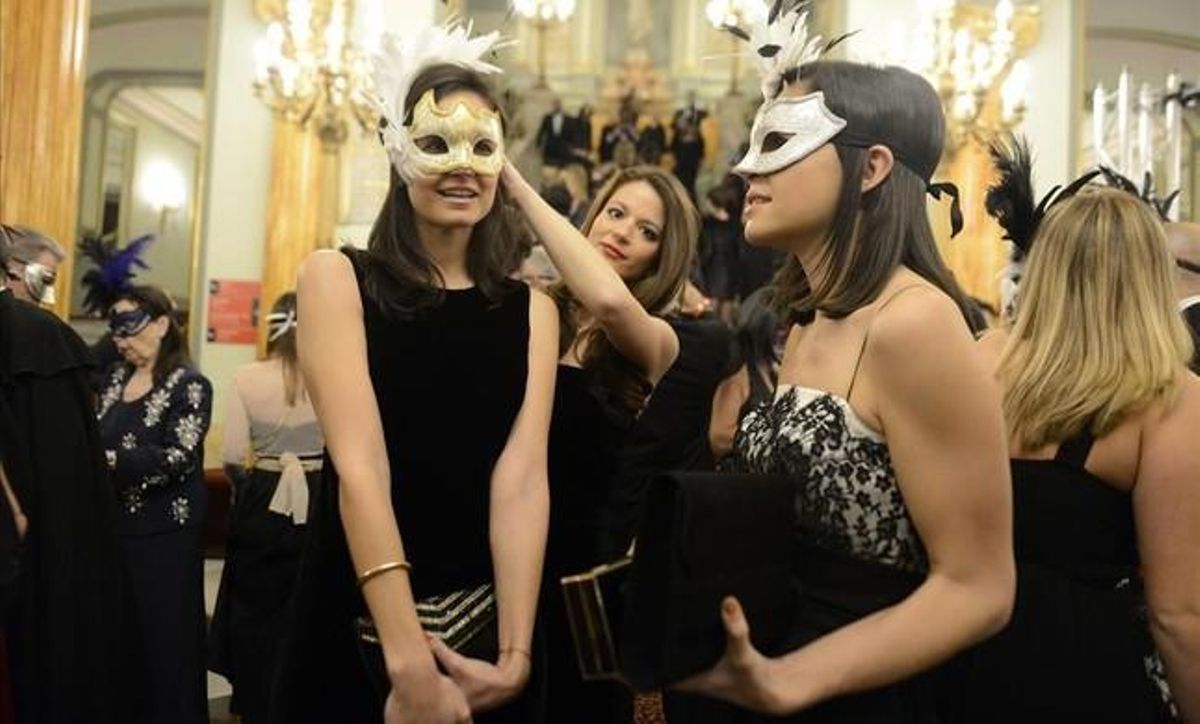 Una chica coloca la máscara a una de sus acompañantes, en la entrada del teatro.