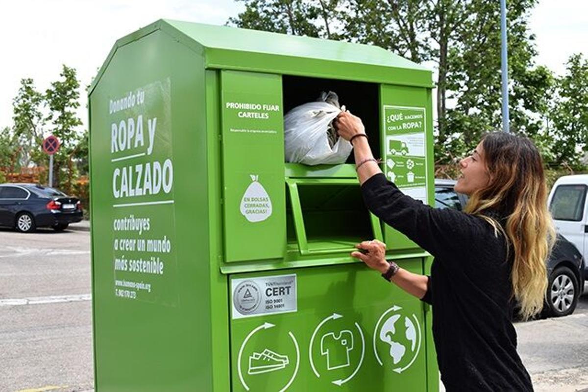 Una mujer tira una bolsa con ropa usada en un contenedor de Humana
