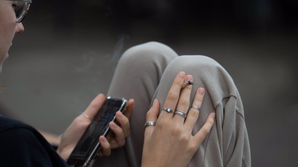 Una joven fuma mientras lee en su móvil.