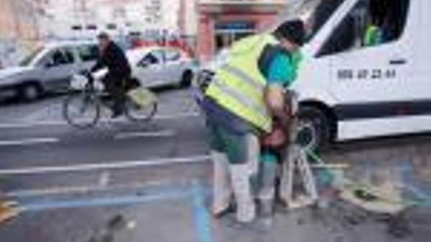 Un ciclista passa pel carril bici mentre un operari treballa per posar les proteccions.