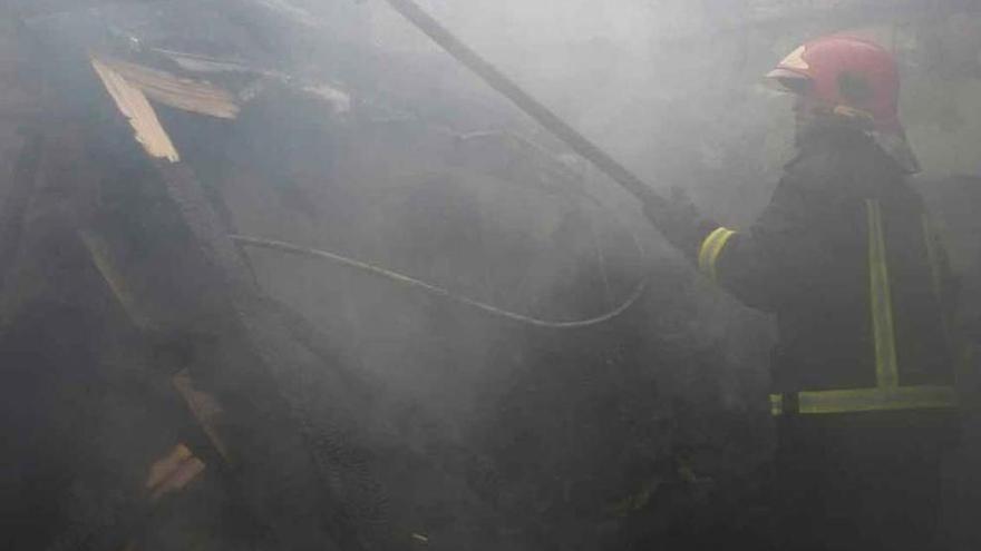 Un bombero retira vigas completamente quemadas del interior de la casa en Villar.