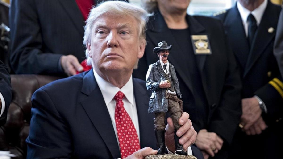 Trump  sostiene una figura con la que ha sido obsequiado en una reunión con los sheriffs del pais en el Despacho Oval de la Casa Blanca  en Washington