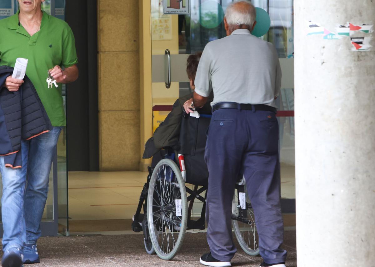 Un hombre empuja la silla de ruedas de una mujer con dependencia en la entrada de un centro de salud.