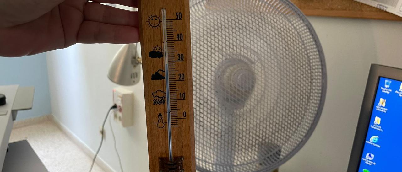Una sanitaria muestra un termómetro que marca 29 grados dentro de una de las consultas, donde hay un ventilador que se han traído de casa para soportar el calor.