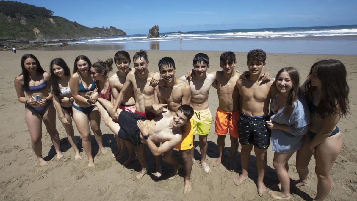 Un grupo de amigos y estudiantes de Soto del Barco y Pravia (con Rodrigo Robledo tumbado e izado por sus amigos), en la playa; al fondo, la peña El Caballar, símbolo de Aguilar. |  MIKI LÓPEZ