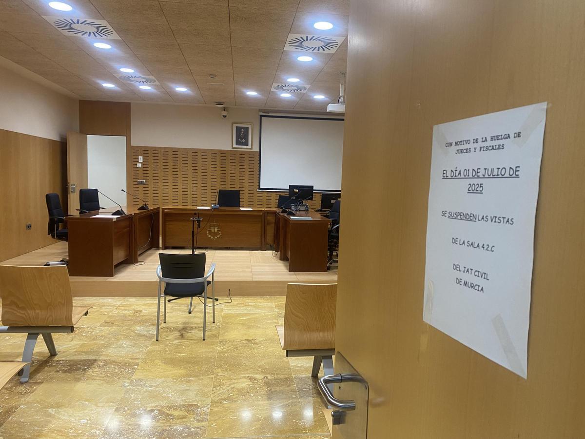Sala de vistas vacía y cartel anunciador de huelga, en verano en la Ciudad de la Justicia de Murcia.