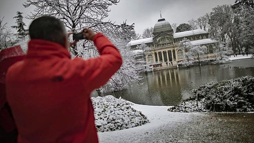 Un hombre hace una foto al Palacio del Cristal del parque del Retiro, en Madrid, completamente nevado