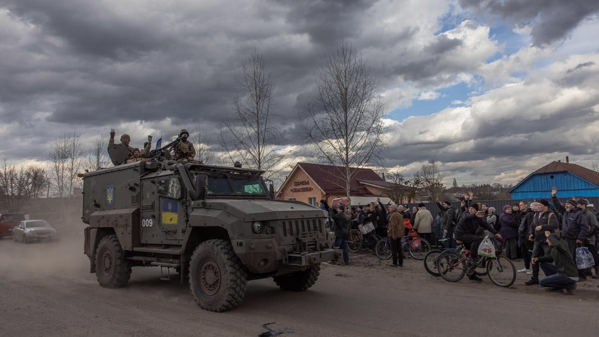 Soldados ucranianos saludan desde un vehículo militar a un grupo de personas que hacen cola para recibir ayuda humanitaria, en el pueblo de Trostyanets, en la región de Sumi.