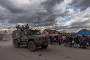 Soldados ucranianos saludan desde un vehículo militar a un grupo de personas que hacen cola para recibir ayuda humanitaria, en el pueblo de Trostyanets, en la región de Sumi.