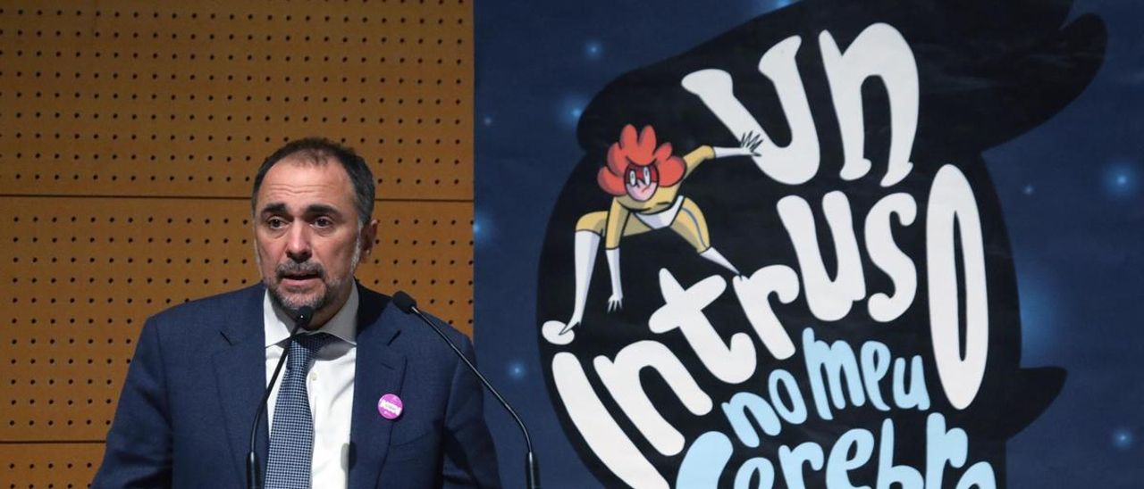 El conselleiro de Sanidade, Julio García Comesaña, delante de la portada del cómic &quot;Un intruso en mi cerebro&quot;.