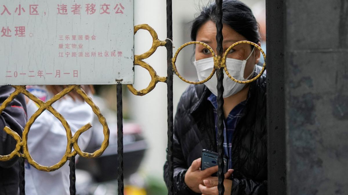 Una mujer espera la entrega de alimentos detrás de una puerta que bloquea la entrada a un área residencial bajo encierro en medio de la pandemia de la enfermedad por coronavirus (COVID-19), en Shanghái, China, el 13 de abril de 2022
