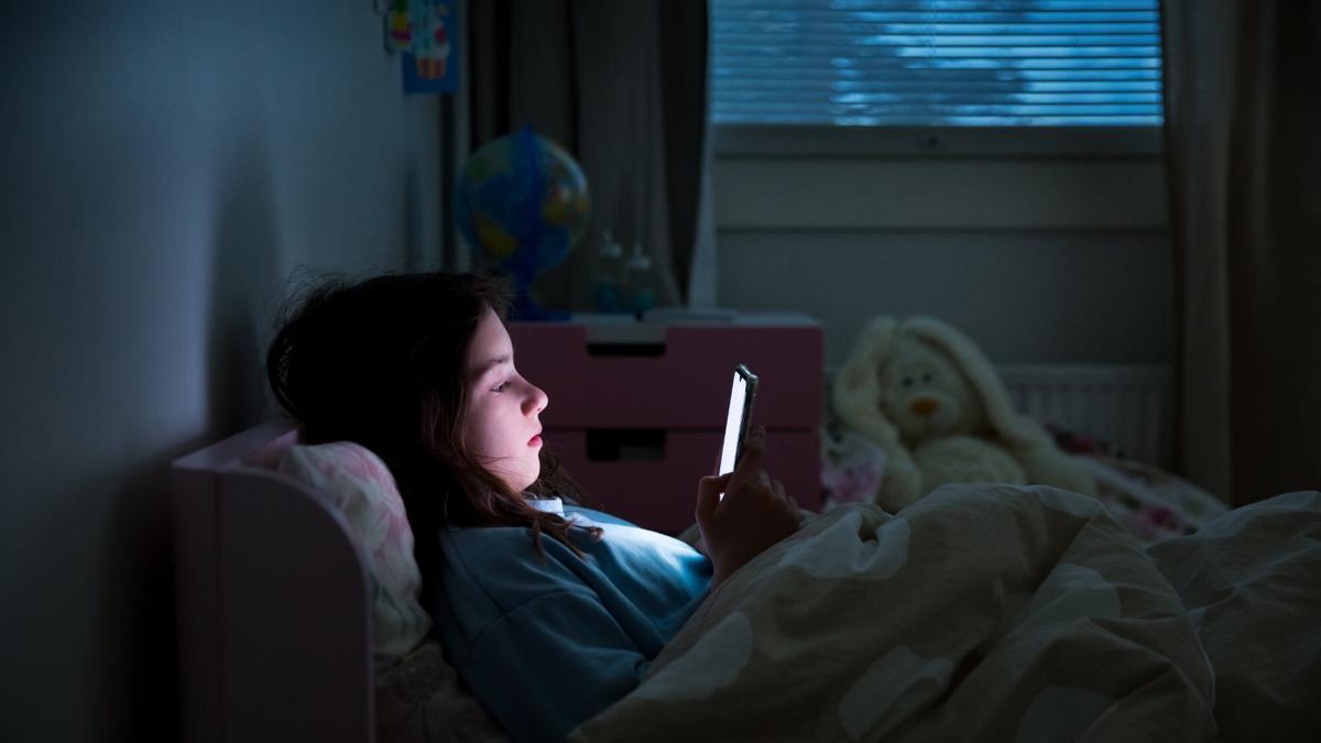 Una niña observa su teléfono móvil en la cama.