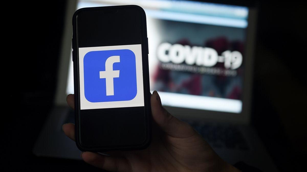 El logo de Facebook en un móvil frente a una pantalla sobre el covid-19.