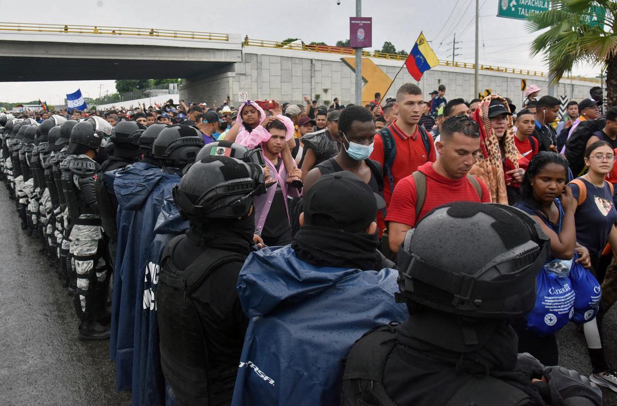 Miembros de la Guardia Nacional montan guardia mientras migrantes de América Central y del Sur con bandera venezolana forman parte de una caravana hacia la frontera con Estados Unidos, en Tapachula, estado de Chiapas, México.