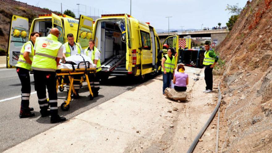 Los sanitarios trasladan a una de las dos heridas en el accidente de Gáldar, con el vehículo volcado al fondo de la imagen. | paco luis mateos