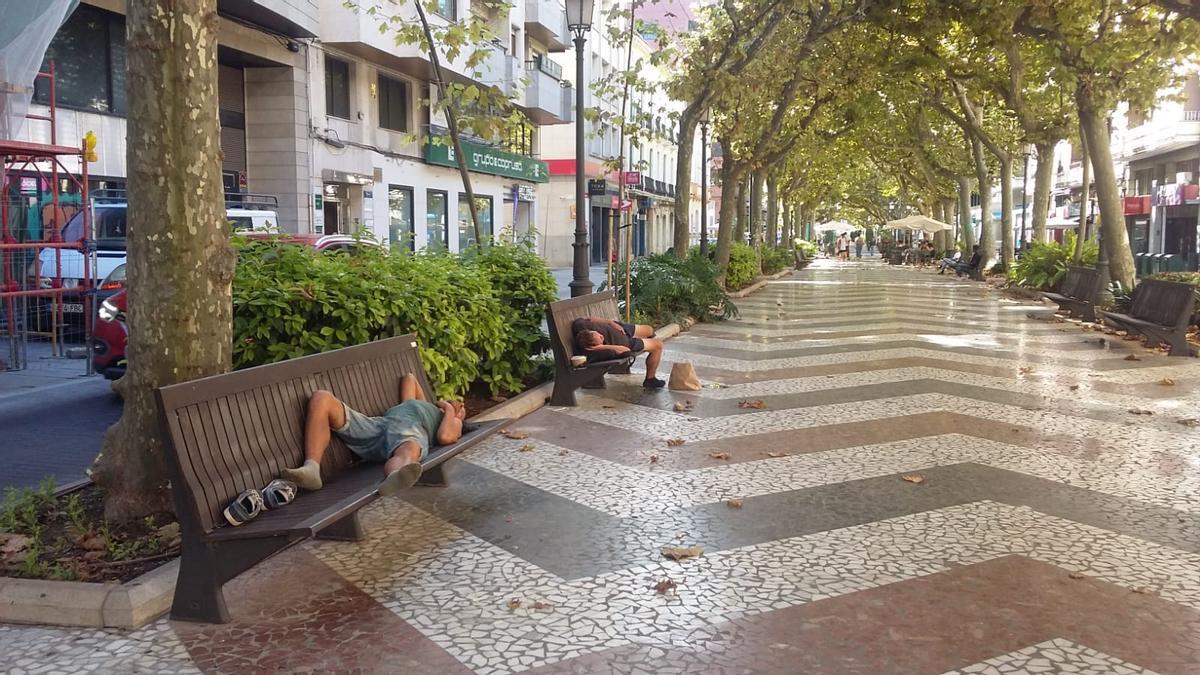 Dos personas durmiendo en sendos bancos del paseo de les Germanies de Gandia