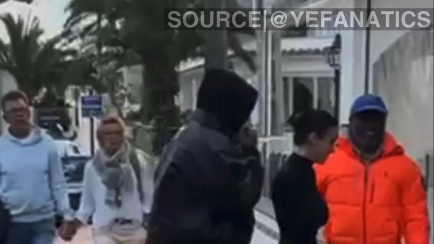 Kanye West, de negro y encapuchado, entrando a un local de Cala d'Or junto a su pareja, Bianca Censori, mientra el productor 88-Keys aguarda en la puerta.