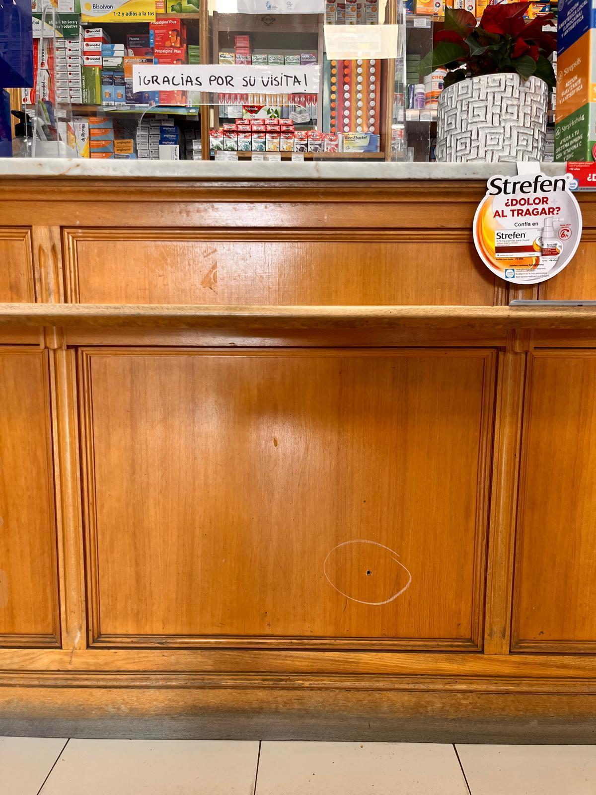 El mostrador de la farmacia, con el impacto de bala y, arriba, el cartel de gratitud.
