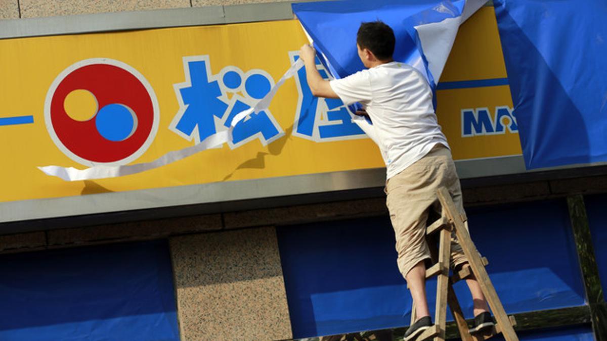 Un trabajador protege el rótulo de un restaurante japonés en Pekín antes de las protestas multitudinarias anunciadas para este martes.