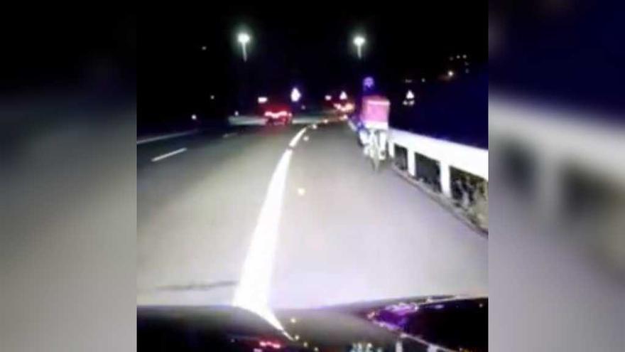 Un repartidor de menjar en bicicieta circulant de nit per l&#039;autopista a Pontevedra