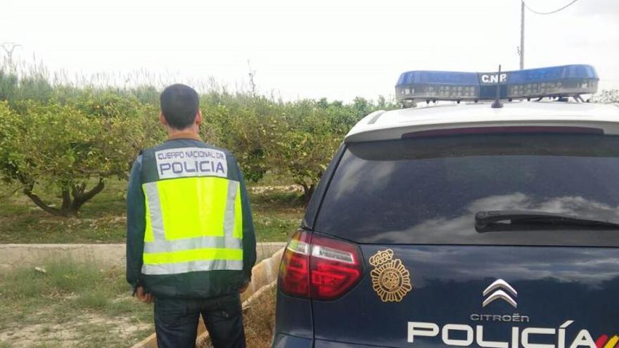 Un agente junto a un coche policial en la zona.