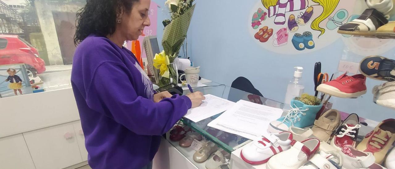 Susana García firma la petición vecinal en la zapatería infantil que regenta en Sama. | M. Á. G.
