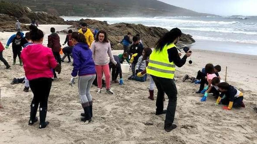 Niños participantes en la limpieza muestran algunos de los restos que recogieron en la playa de Caión.