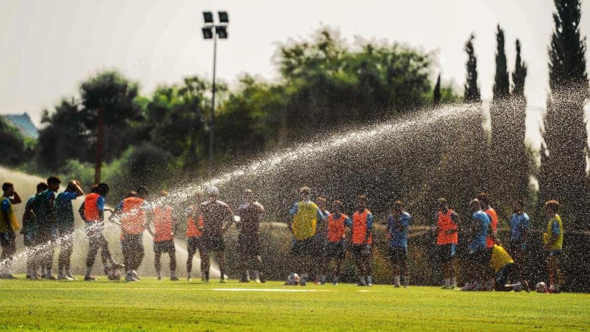 Un aspersor riega Fontcalent mientras la plantilla escucha al entrenador antes de iniciar la sesión preparatoria del Hércules, en Alicante.