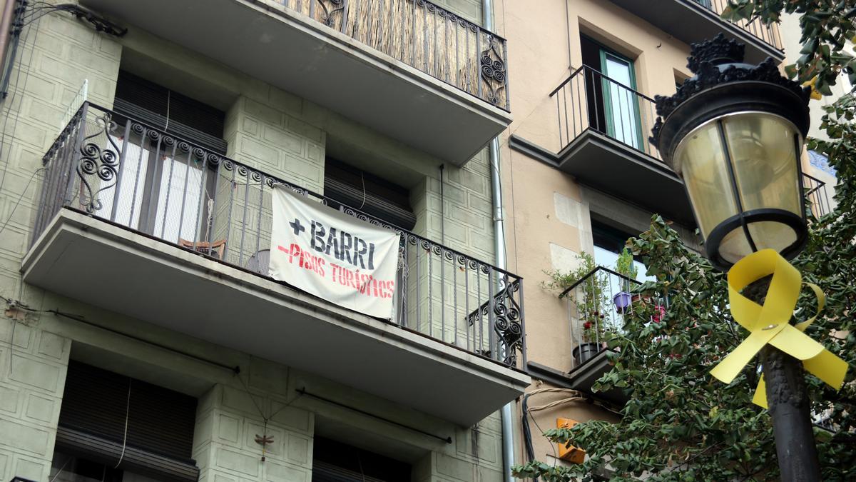 Un cartell amb el lema &#039;+Barri -Pisos Turístics&#039; penjat en un balcó de la Rambla de Girona