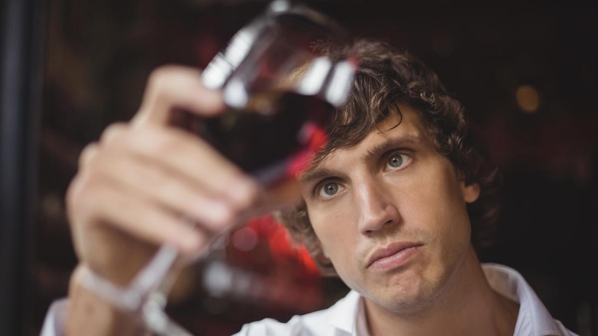 Camarero mirando una copa de vino tinto en la barra del bar