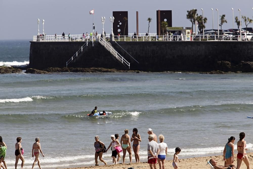 Gijoneses y visitantes se lanzan a la playa en una jornada calurosa.